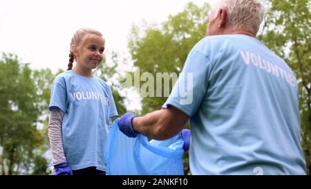 Female child putting garbage in plastic bag helping grandfather, togetherness Stock Photo