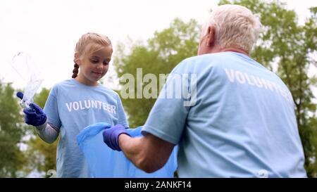 Grandfather holding plastic bag, happy girl putting waste in garbage, generation Stock Photo