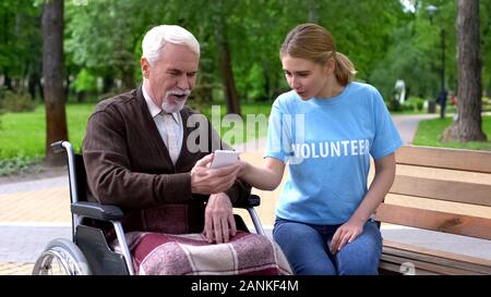 Female volunteer teaching handicapped man use smartphone, relaxing at park Stock Photo