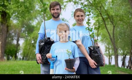 Parents and child in volunteer t-shirts holding potted trees nature conservation Stock Photo