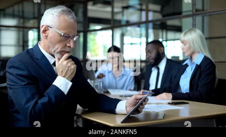 Mature businessman thinking of decision looking tablet, managers discussing plan Stock Photo