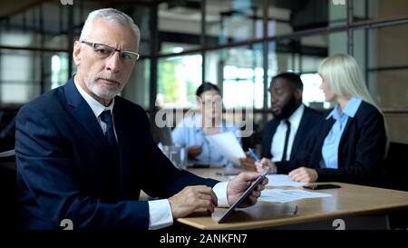Concerned company boss making decision tablet in hands, managers discussing plan Stock Photo