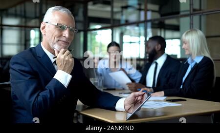 Successful company boss smiling, tablet in hands, colleagues discussing business Stock Photo