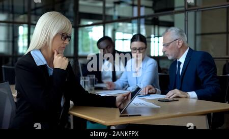 Thoughtful female boss analyzing tablet report, business colleagues in office Stock Photo