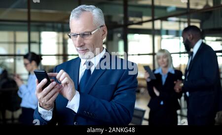 Mature male boss using smartphone, texting business partner, using mobile app Stock Photo
