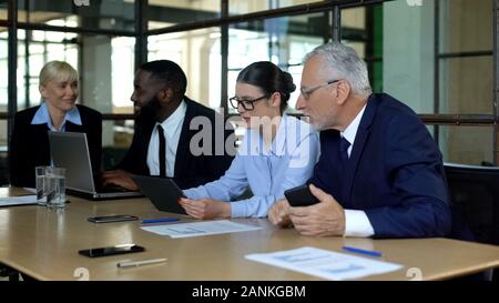 Company colleagues discussing news in office, using modern gadgets, teamwork Stock Photo
