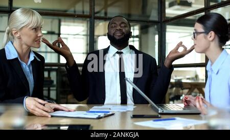 Businessman meditating in office, tired of female colleagues conflict at work Stock Photo