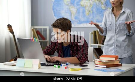 Angry mother shouting son playing laptop game instead doing homework, discipline Stock Photo