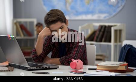 Teenager looking at piggybank on table sitting home, dreaming purchase, budget Stock Photo