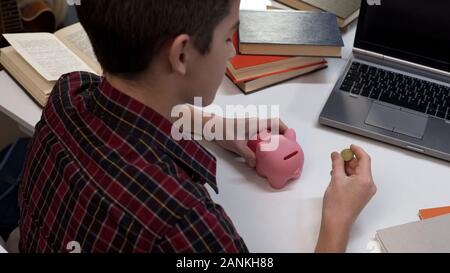 Teenager holding coin going to put into piggy bank, saving money, finances Stock Photo