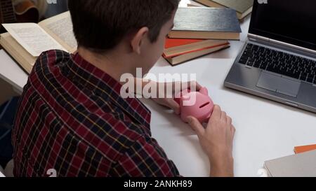 School pupil holding pink piggybank in hands, saving pocket money, economy Stock Photo