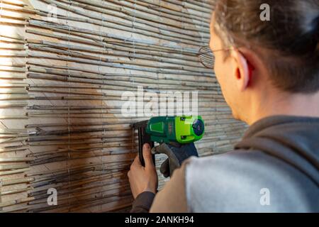 Man is fixating reed mats on a wooden wall to prepare them for plastring the walls with clay and sand - concept of modern and ecological architecture Stock Photo