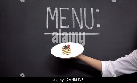 Hand holds plate with cake on Menu background, delicious desserts in restaurant Stock Photo