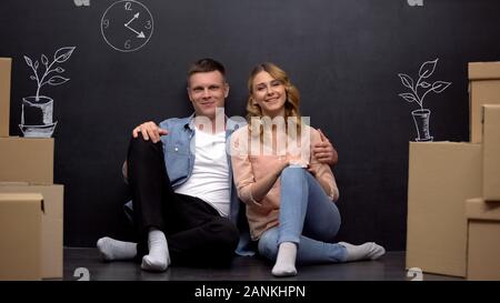 Young smiling couple in new apartment, cartoon boxes in empty room, moving Stock Photo