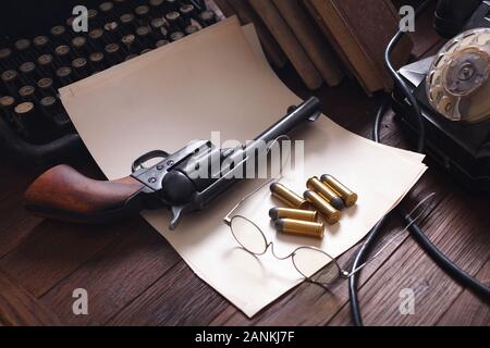 Old retro vintage typewriter with revolver and blank sheet of paper on wooden table