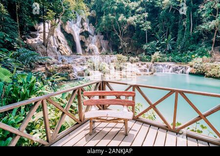 Panoramic view over Kuang Si waterfall close to Luang Prabang, Laos. Water motion effect, bench on the foreground Stock Photo