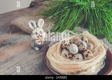 Spring composition with a wicker nest of straw, green grass, decorative hare and Easter quail eggs on a simple wooden background Stock Photo