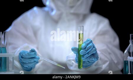 Scientist in protective suit taking liquid sample from test tube with radiation Stock Photo
