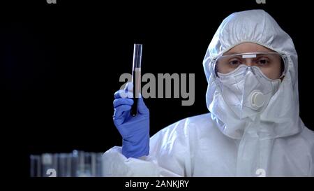 Female researcher in protective suit showing oil liquid in test tube, poison Stock Photo