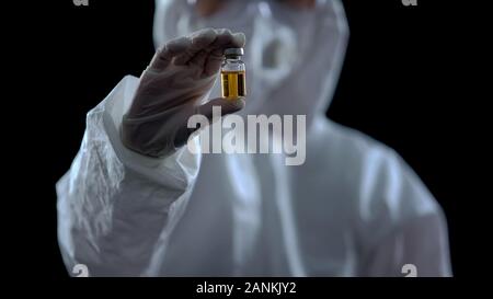 Epidemiologist showing bottle with yellow liquid, vaccine development, treatment Stock Photo