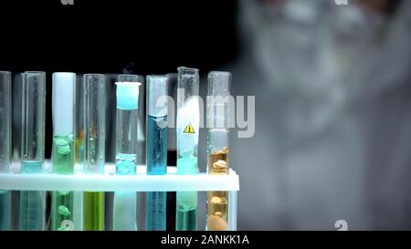 Researcher looking at test tubes with colorful liquids in lab, warning symbol Stock Photo
