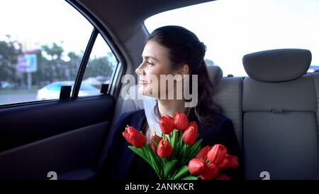 Pretty lady sitting on backseat and holding tulips, successful date, happiness Stock Photo