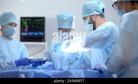 Assistant giving surgeon sterile medical equipment, invasive hospital operation Stock Photo