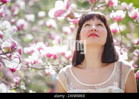 girl looks up. beautiful woman against background of magnolia flowers. Stock Photo