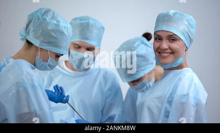 Professional surgeon team working in operation room, nurse smiling at camera Stock Photo