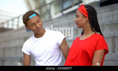 Teenager boy looking at offended girlfriend, trying to make peace after quarrel Stock Photo