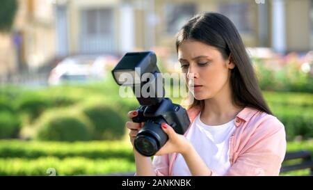 Serious female photographer checking settings on camera, technique problems Stock Photo