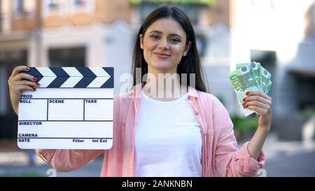 Woman showing clapperboard and bunch of euros at camera, film production worker Stock Photo