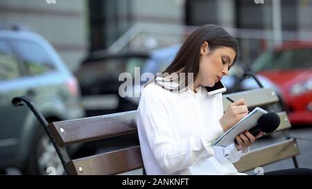 Female journalist making notes and talking phone, preparing for reportage Stock Photo