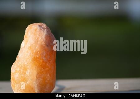 Blurred outdoor background with a closeup of a himalayan salt rock on a wood table in the summer sunlight Stock Photo