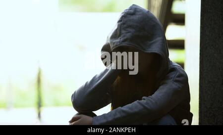 Melancholic teen female in hoodie touching face with palm, suffering depression Stock Photo