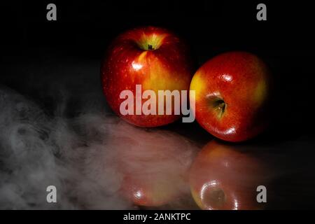 A low key image of two golden and red apples  on a highly reflective surface against a black background surrounded by a low fog with plenty of room fo Stock Photo