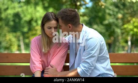 Young male supporting sad girlfriend sitting park bench together, loving spouse Stock Photo