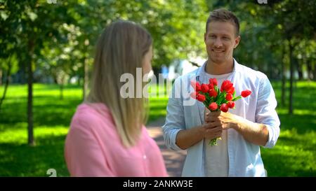 Smiling handsome man with red tulips looking girlfriend, romantic date present Stock Photo
