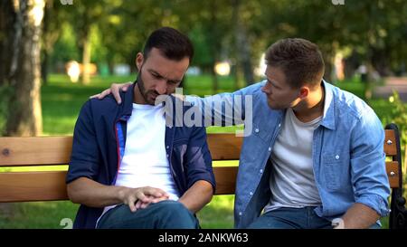Young male supporting friend sitting outdoors together, friendship care, advice Stock Photo