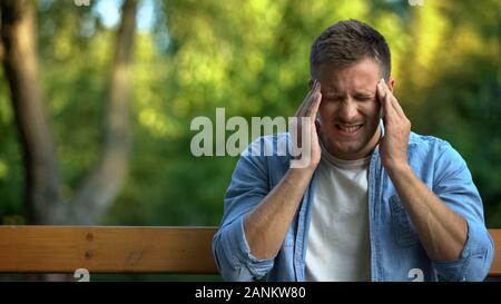 Young sick male suffering headache sitting outdoors, migraine symptom, health Stock Photo
