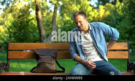 Male sitting on bench suffering from lover back pain after trauma or injury Stock Photo