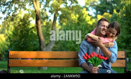 Happy young woman hugging boyfriend holding red tulips in hands, outdoor date Stock Photo