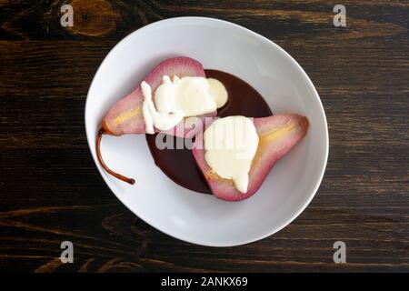 Red Wine Poached Pears with Dark Chocolate & Vanilla Cream: Bosc pear poached in red wine, sliced in half, and served with chocolate sauce Stock Photo