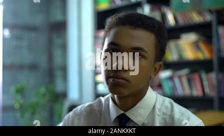 Upset tired black student in uniform sighing and sadly looking on cam, laziness Stock Photo