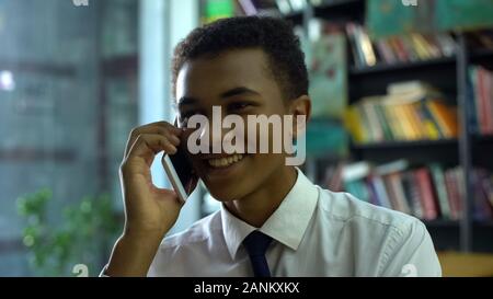 Cheerful afro-american male student chatting cellphone during homework doing Stock Photo