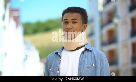 Upset afro-american teen boy in foam cervical collar sadly sighing on cam trauma Stock Photo