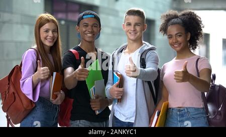 Smiling multiethnic students with notebooks showing thumbs up, college choice Stock Photo