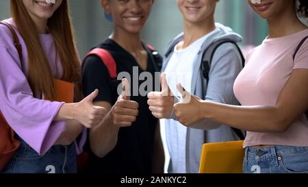 Happy mixed-race friends with books showing thumbs up, student exchange program Stock Photo