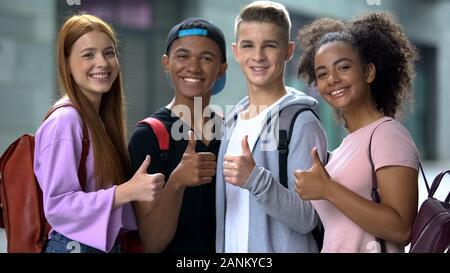 Group of multiethnic students with backpacks showing thumbs-up, education Stock Photo