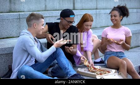 Happy multiethnic teen friends eating pizza academy stairs, having fun together Stock Photo